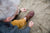 Man tying Aurora Shoe Co. North Pacific Handmade Leather Shoes on sandy beach, wearing mustard khaki pants.