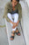 Woman sitting on stone steps, wearing green jacket, white pants, and black New Mexican handmade leather sandals by Aurora Shoe Co.