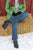 Woman sitting on straw bale, in front of red barn, in snow, wearing scar, green jacket, blue jeans, and Middle English Aurora Shoe Co. Handmade Leather Shoes