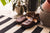 Aurora Shoe Co. Brown T-strap leather shoes inside on floor with striped rug and green plant in background.