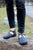 Woman standing on stone wearing black pants and black t-strap handmade leather shoes by Aurora Shoe Co.