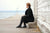 Woman sitting at Wells College Dock, overlooking Cayuga Lake, wearing black coat, black stockings, black T-strap Aurora Shoe Co. handmade leather shoes.