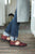 Woman wearing rolled blue jeans, grey apron, standing on wool rug, wearing burgundy T-Strap Aurora Shoe Co. Handmade Leather Shoes.