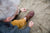 Man tying Aurora Shoe Co. North Pacific Handmade Leather Shoes on sandy beach, wearing mustard khaki pants.