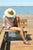 Woman, sitting on wooden bench on wooden dock at Cayuga Lake, wearing sun hat, white shirt, pink shorts, and burgundy New Mexican Handmade leather shoes by Aurora Shoe Co.