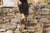 Model sitting on old stone wall with black shirt, black pants, Middle English Handmade Leather Aurora Shoe Co. Shoes in olive color.