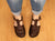Woman wearing rolled, worn blue jeans and Aurora Shoe Co. Brown T-strap leather handmade leather shoes without socks.