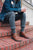 Man sitting on brick steps, wearing jean jacket, rolled pants, grey socks, and brown North Pacific handmade leather boots by Aurora Shoe Co.